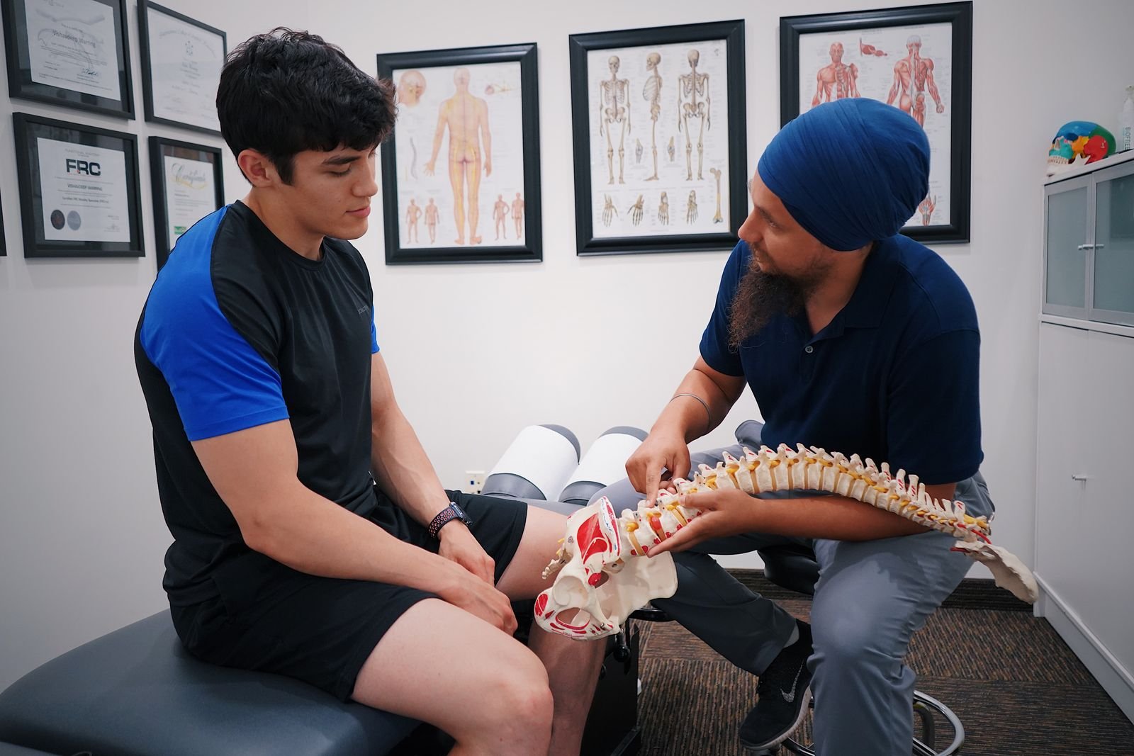 A chiropractor explaining a spine model to a patient — diagnosis before treatment